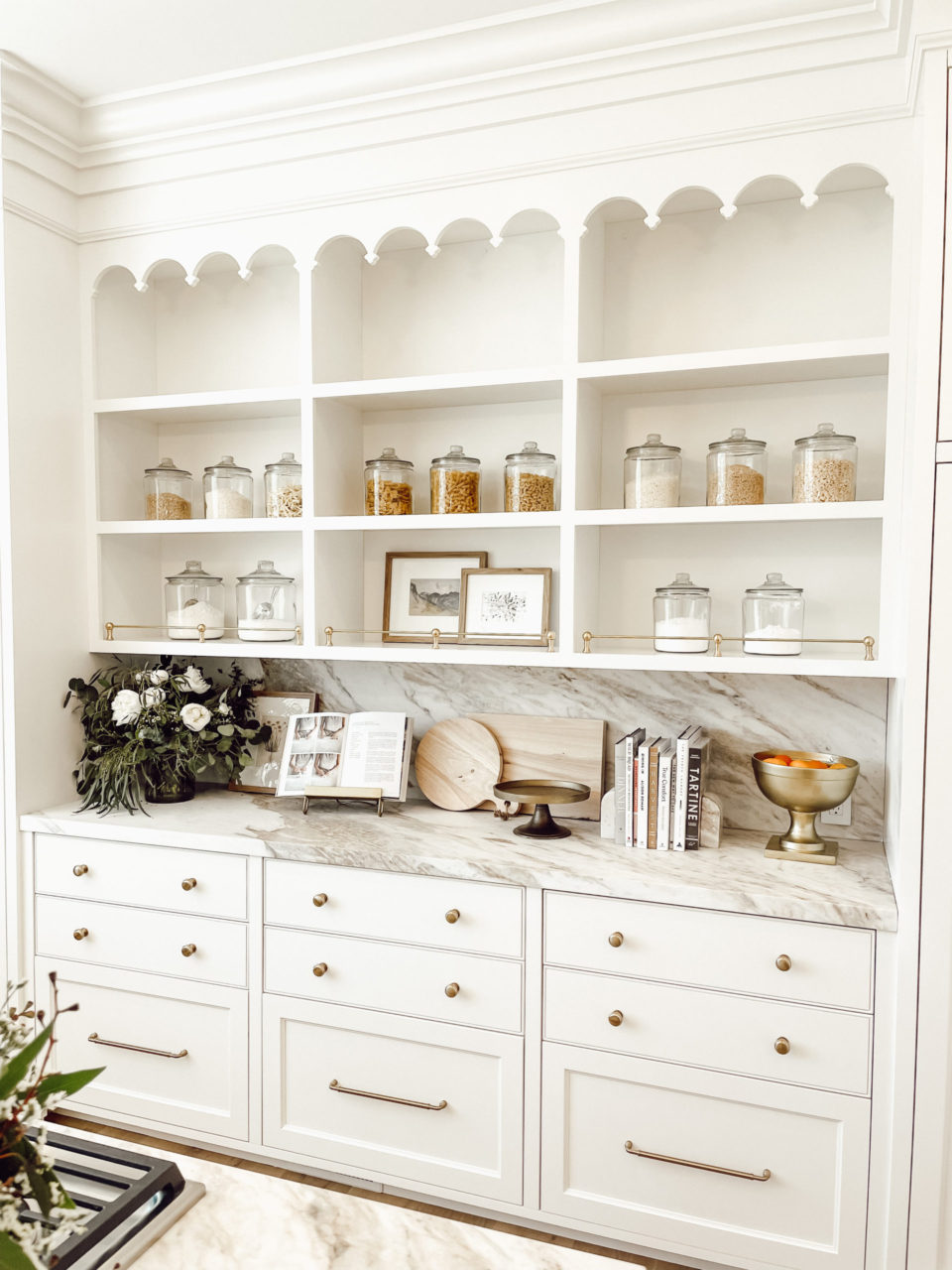 pantry with glass jars, white cabinets and gold hardware. intricate molding detail